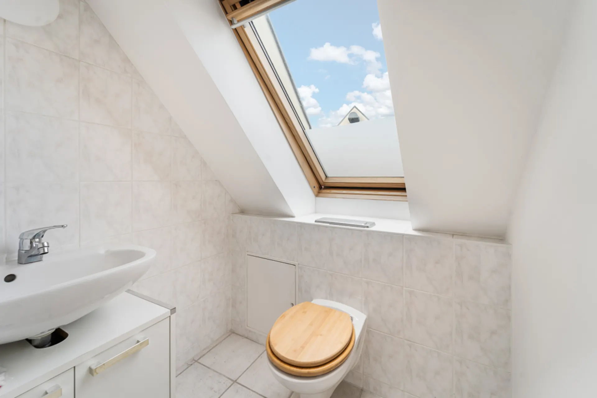 Kleines Badezimmer mit Waschbecken, Toilette und Dachfenster mit Blick auf den Himmel.