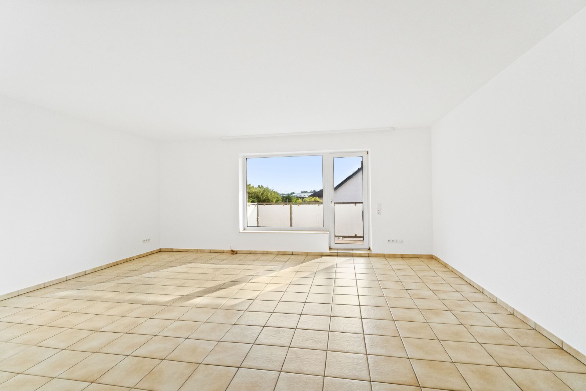 Leerer Raum mit hellen Fliesen, weißen Wänden und großem Fenster mit Tür nach draußen.