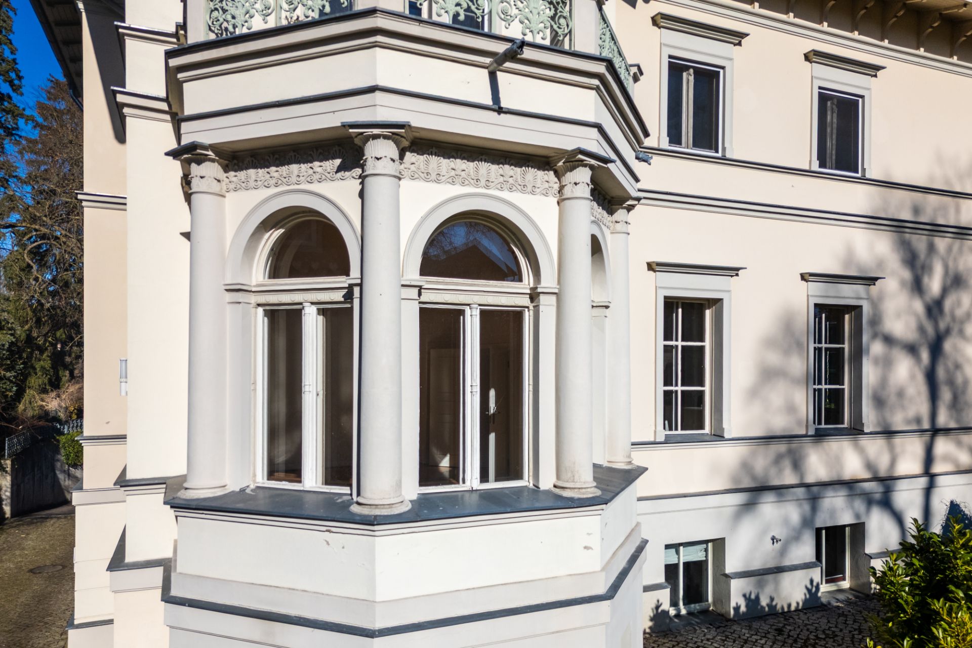 Erker mit Rundbogenfenstern und Säulen an einer hellen Hausfassade.