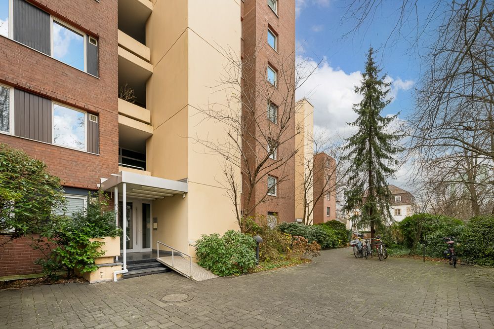 Eingang eines mehrstöckigen Wohnhauses mit Pflanzen und Fahrrädern davor.