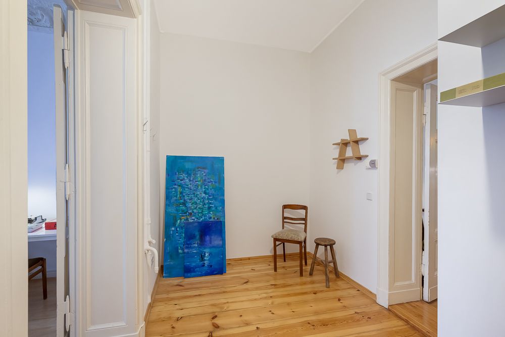 Heller Flur mit Holzfußboden, Stuhl, Hocker, Wandregal und blauem Gemälde an der Wand.