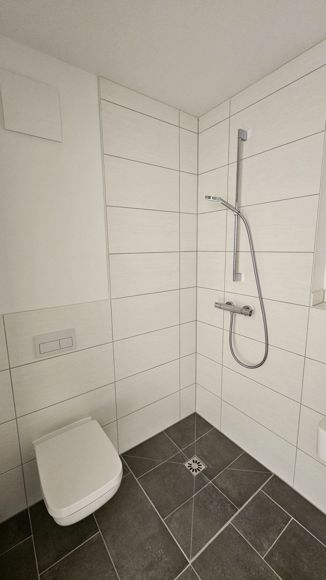 Modernes Bad mit bodengleicher Dusche und WC, weiße Wandfliesen, dunkle Bodenfliesen.