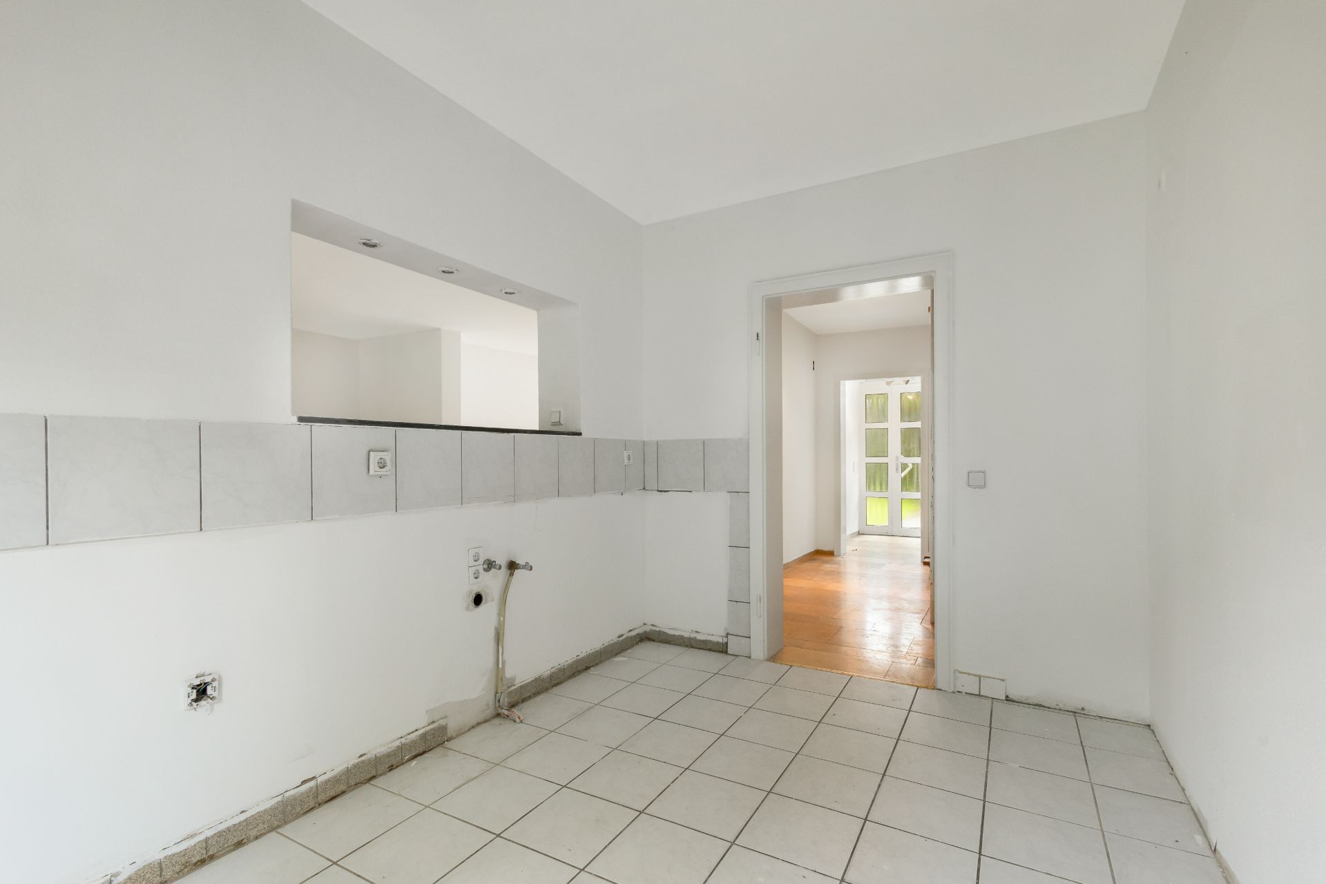 Leerer, gefliester Raum mit Wanddurchbruch und Blick in einen weiteren Raum mit Holzboden.