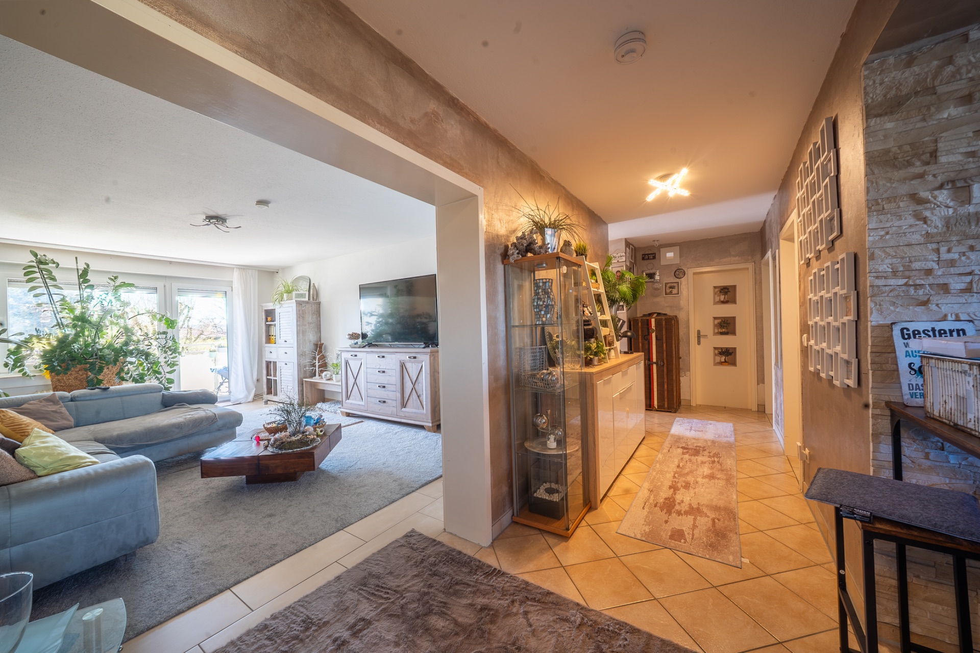 Heller Flur mit Teppich, Blick ins Wohnzimmer mit Sofa, Couchtisch und großen Fenstern.
