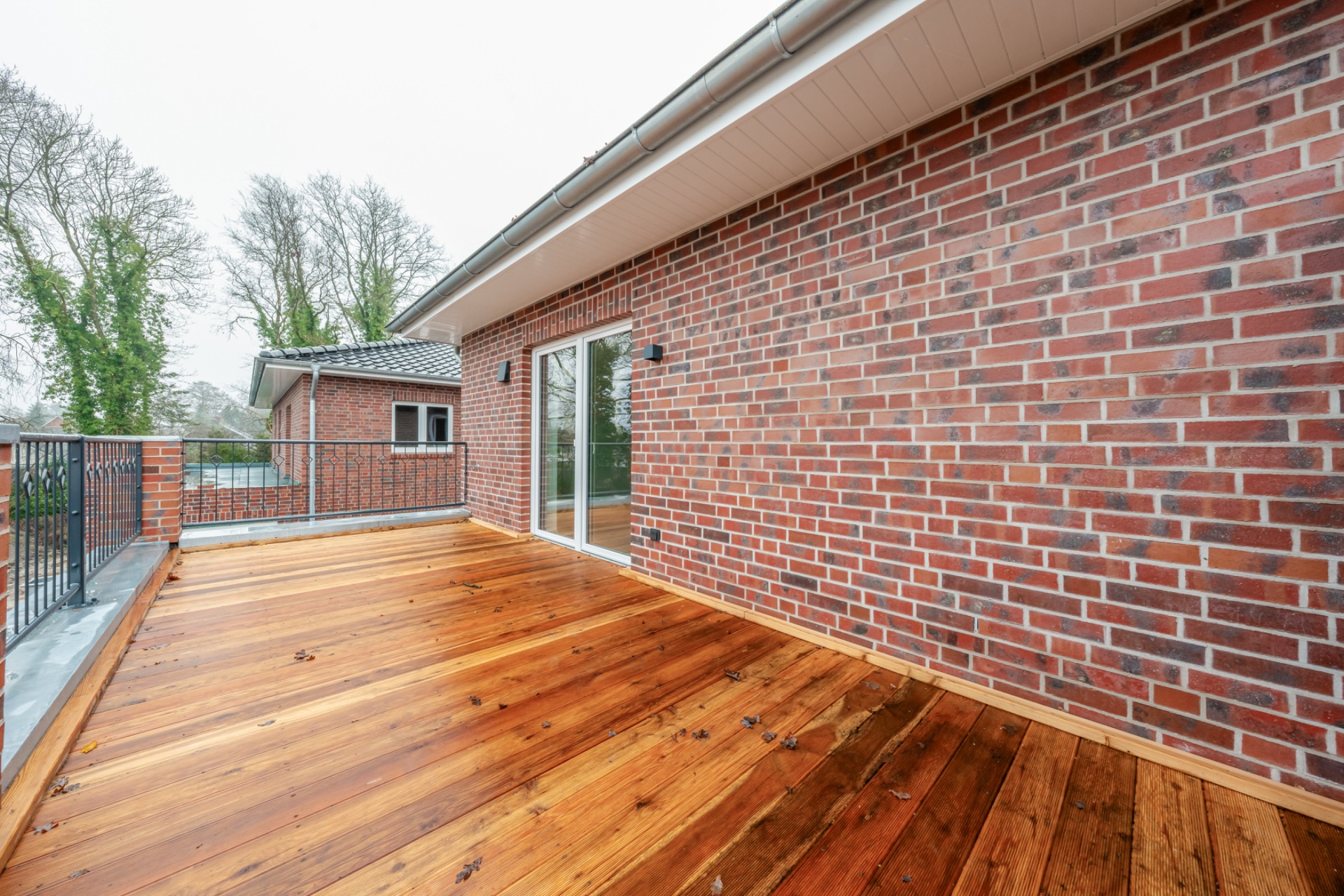 Große Holzterrasse mit Geländer und Zugang zu einem Backsteinhaus.
