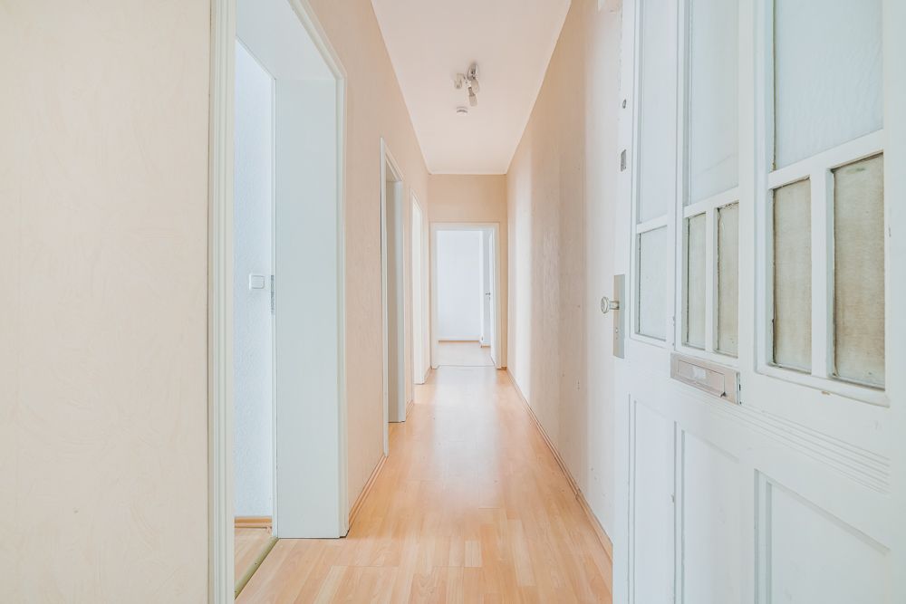 Heller Flur mit Holzboden, weißen Türen und beigen Wänden in einer Wohnung.