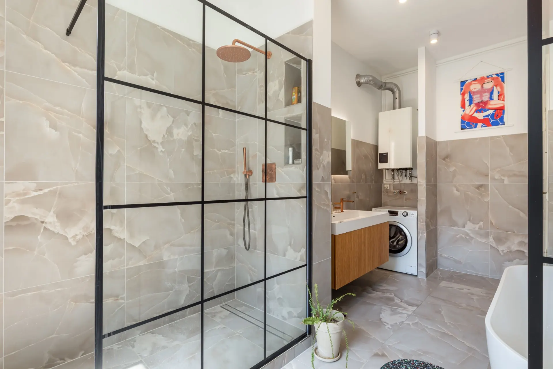 Modernes Badezimmer mit großer Glasdusche, Waschbecken, Waschmaschine und grauen Fliesen.