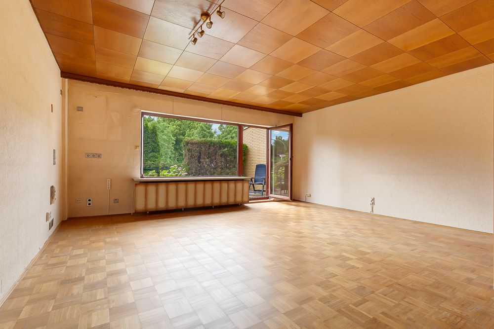 Leeres Wohnzimmer mit Parkettboden, Holzdecke und großem Fenster zur Terrasse.