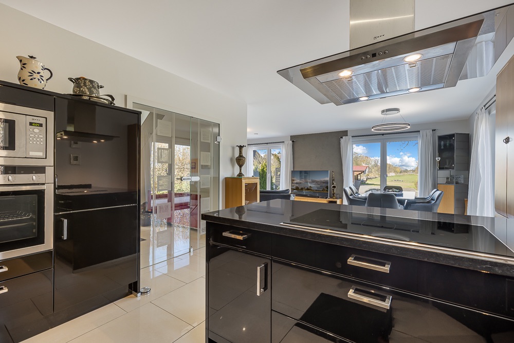 Moderne schwarze Einbauküche mit offenem Blick ins helle Wohnzimmer und Essbereich mit großen Fenstern.