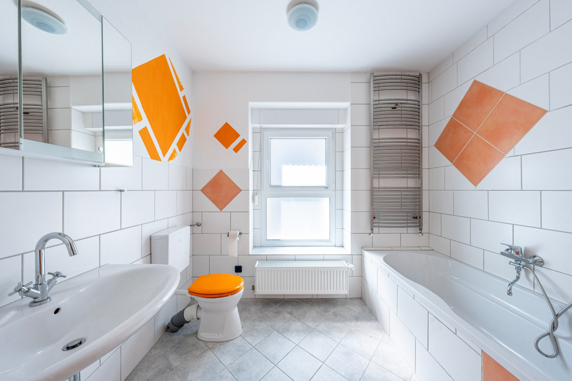 Modernes Badezimmer mit Badewanne, Waschbecken und Toilette mit orangefarbenem Sitz.