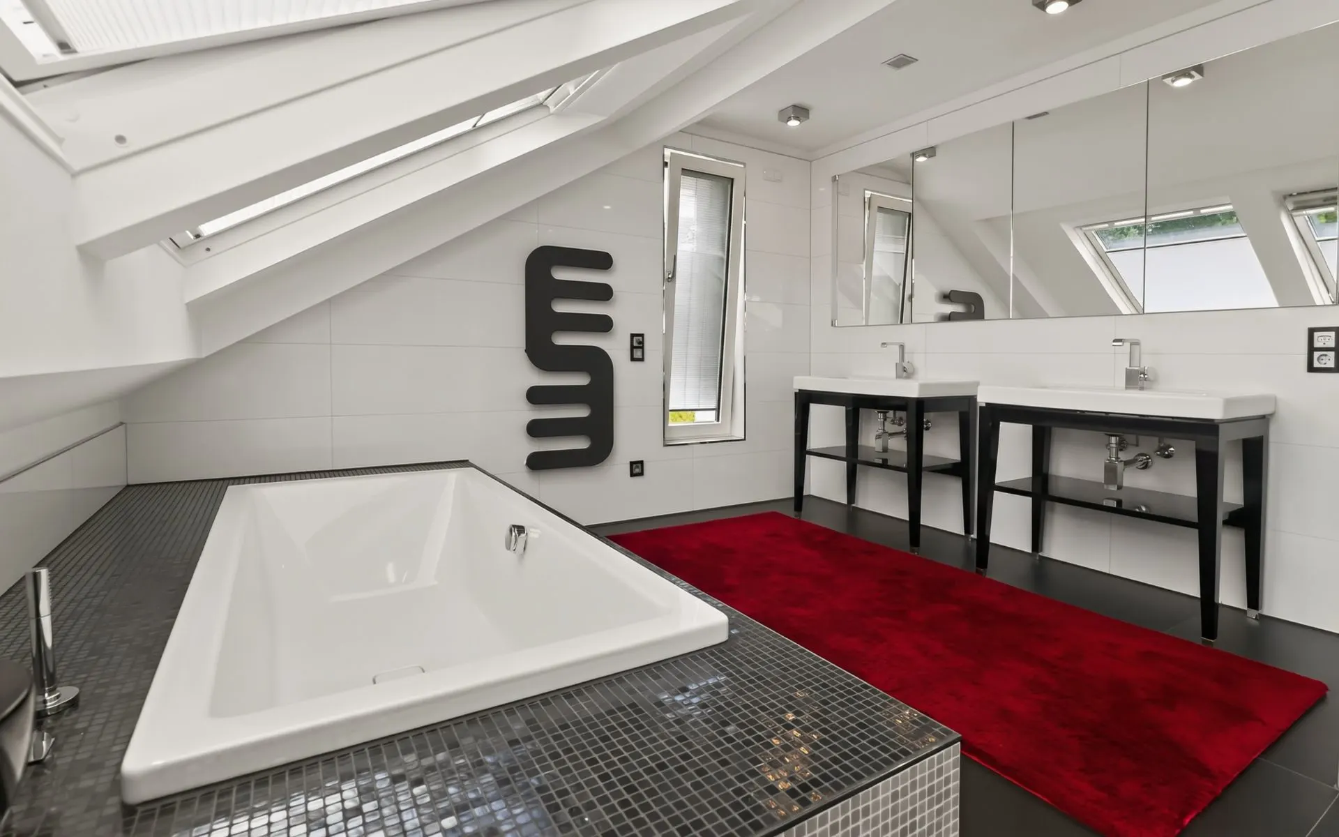Modernes Badezimmer mit Badewanne, zwei Waschbecken, großem Spiegel und rotem Teppich unter Dachschräge.