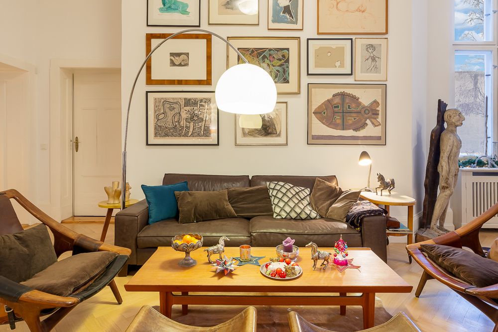 Wohnzimmer mit braunem Sofa, Holzsesseln, großem Tisch und vielen Bildern an der Wand.