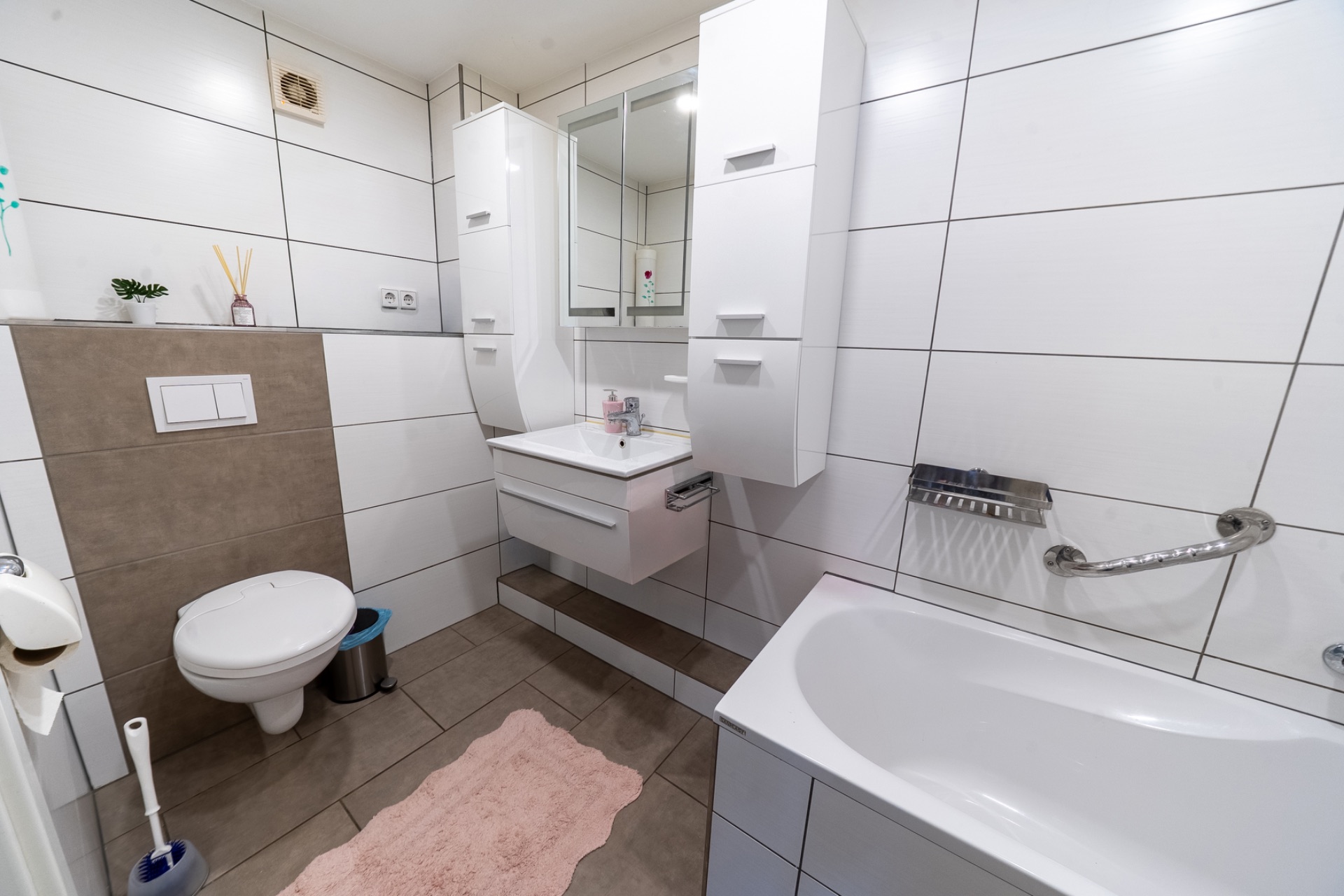 Modernes Bad mit Badewanne, Wand-WC, Waschbecken, Spiegel und weißen Fliesen.