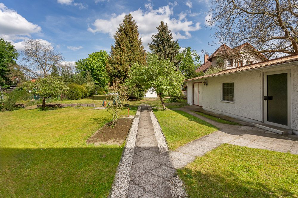 Gepflegter Garten mit Rasen, Bäumen und gepflastertem Weg neben einem weißen Haus.