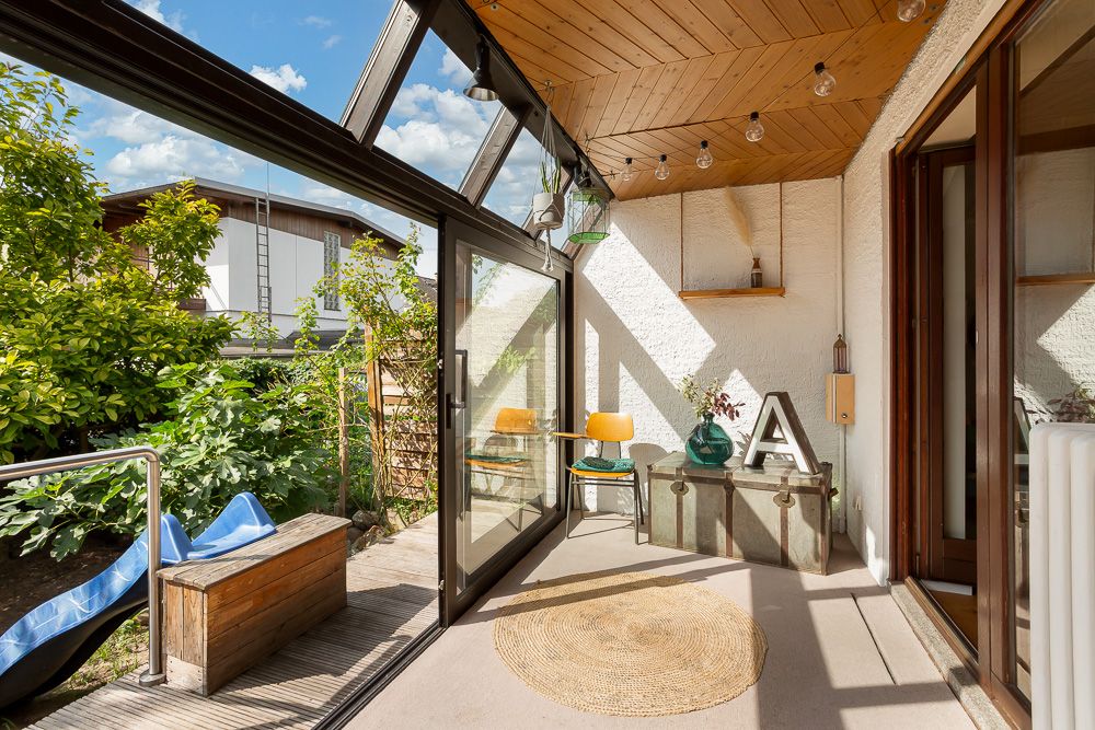 Heller Wintergarten mit Glastüren, Holzboden, Deko und Blick auf den Garten.
