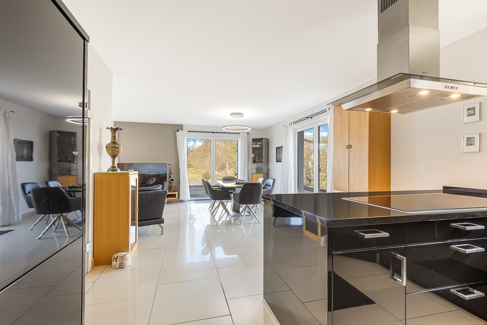 Moderne offene Küche mit Essbereich und Wohnzimmer, große Fenster mit Blick nach draußen.