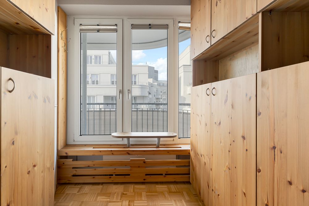 Heller Raum mit großen Fenstern, Holzschränken und Blick auf einen Balkon.