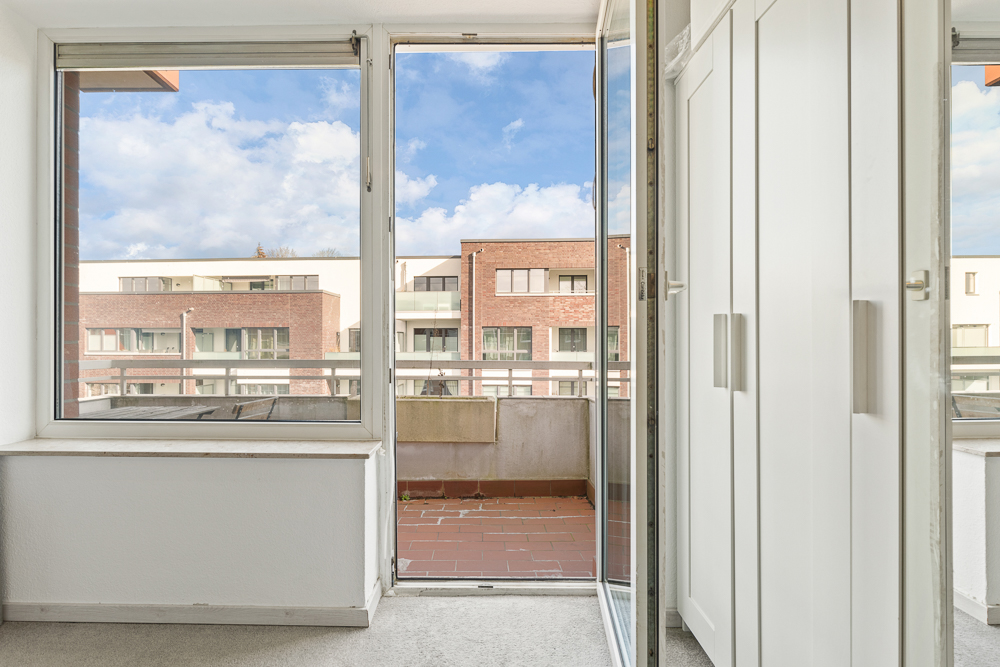 Offene Balkontür mit Blick auf Balkon, Nachbarhäuser und weißen Kleiderschrank rechts.