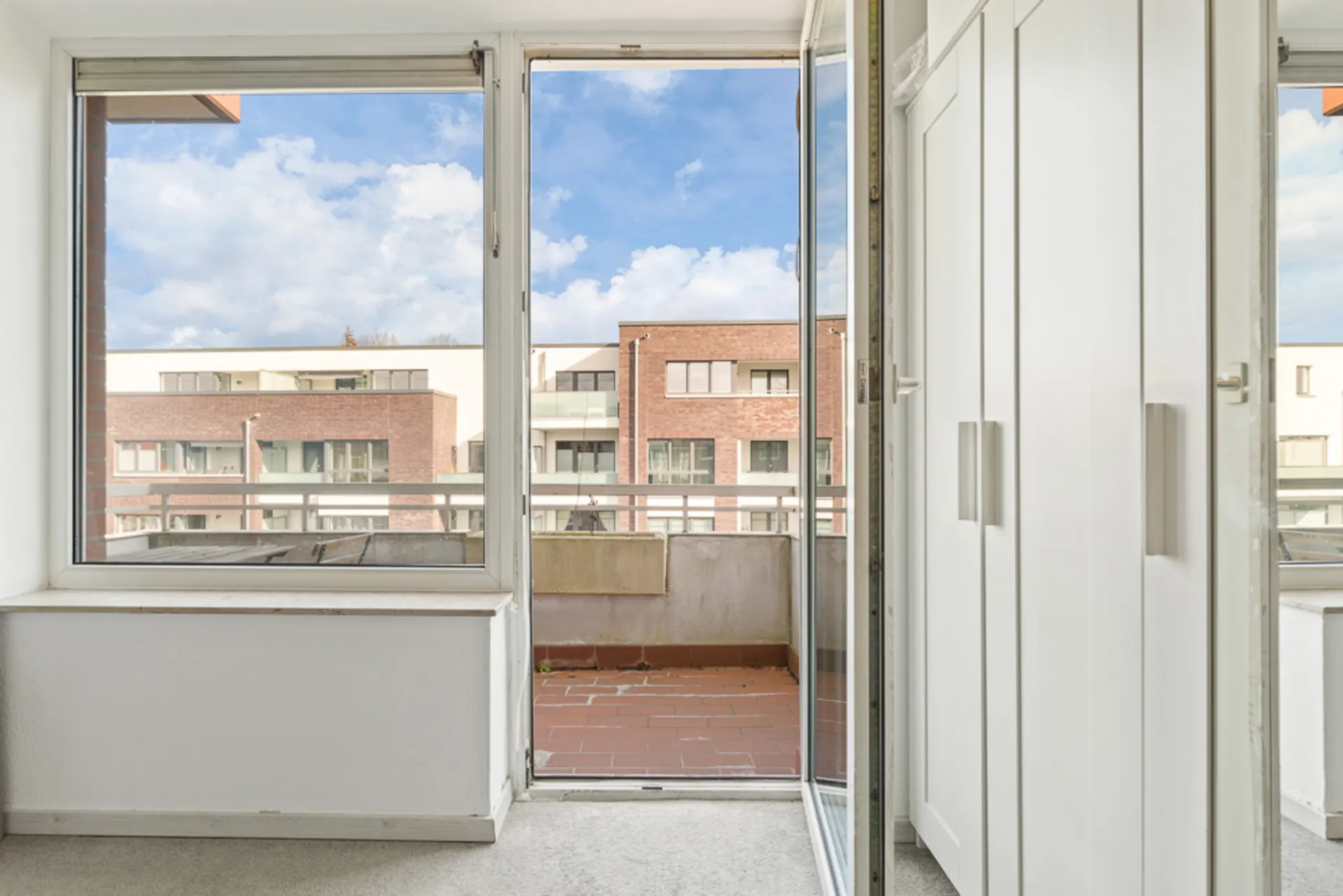 Offene Balkontür mit Blick auf Balkon, Nachbarhäuser und weißen Kleiderschrank rechts.