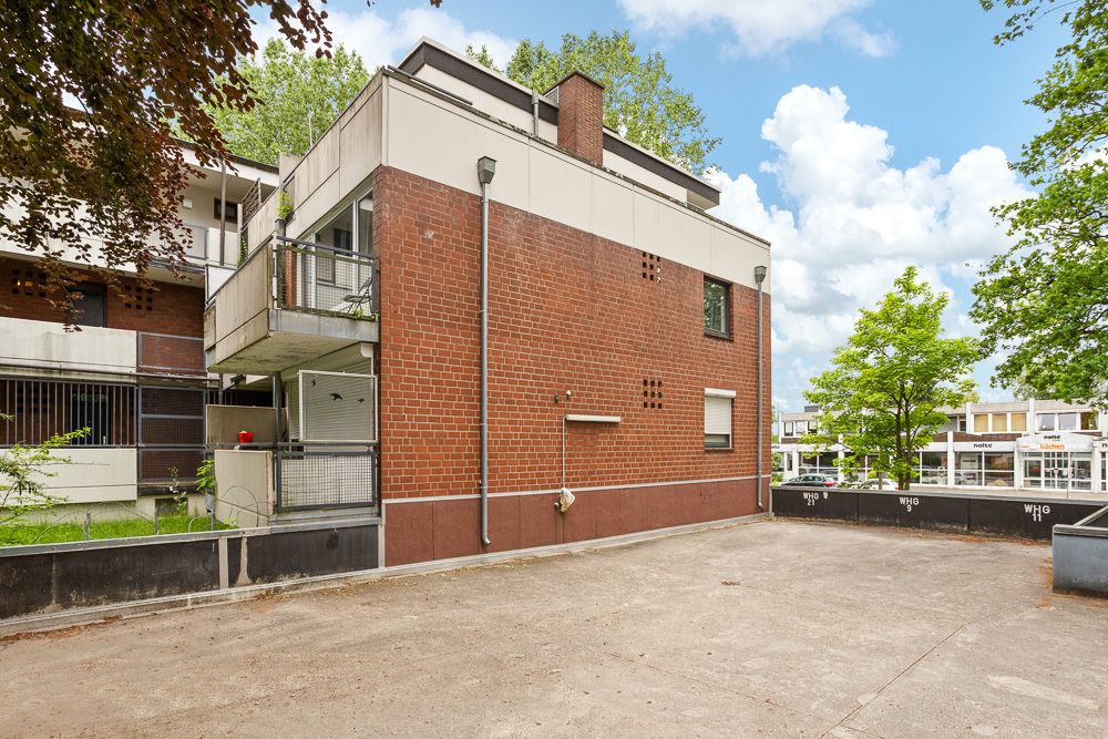 Mehrfamilienhaus mit Backsteinfassade, Balkonen und großem gepflastertem Vorplatz.