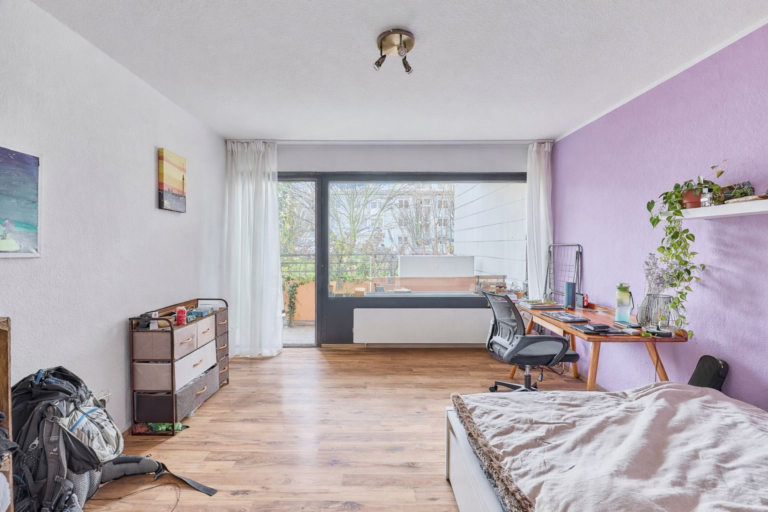 Helles Zimmer mit Bett, Schreibtisch, Regal, Holzboden und großem Fenster zur Terrasse.