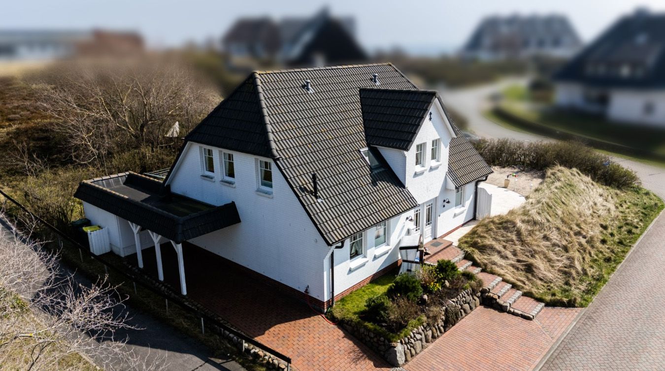 Weißes Einfamilienhaus mit dunklem Dach, Vorgarten und Auffahrt in ruhiger Wohngegend.