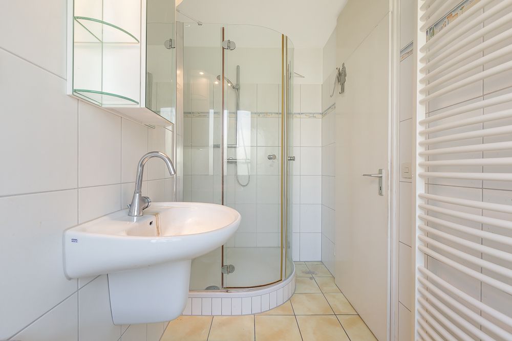 Modernes Badezimmer mit Glasdusche, Waschbecken, beleuchtetem Spiegel und Handtuchheizkörper.