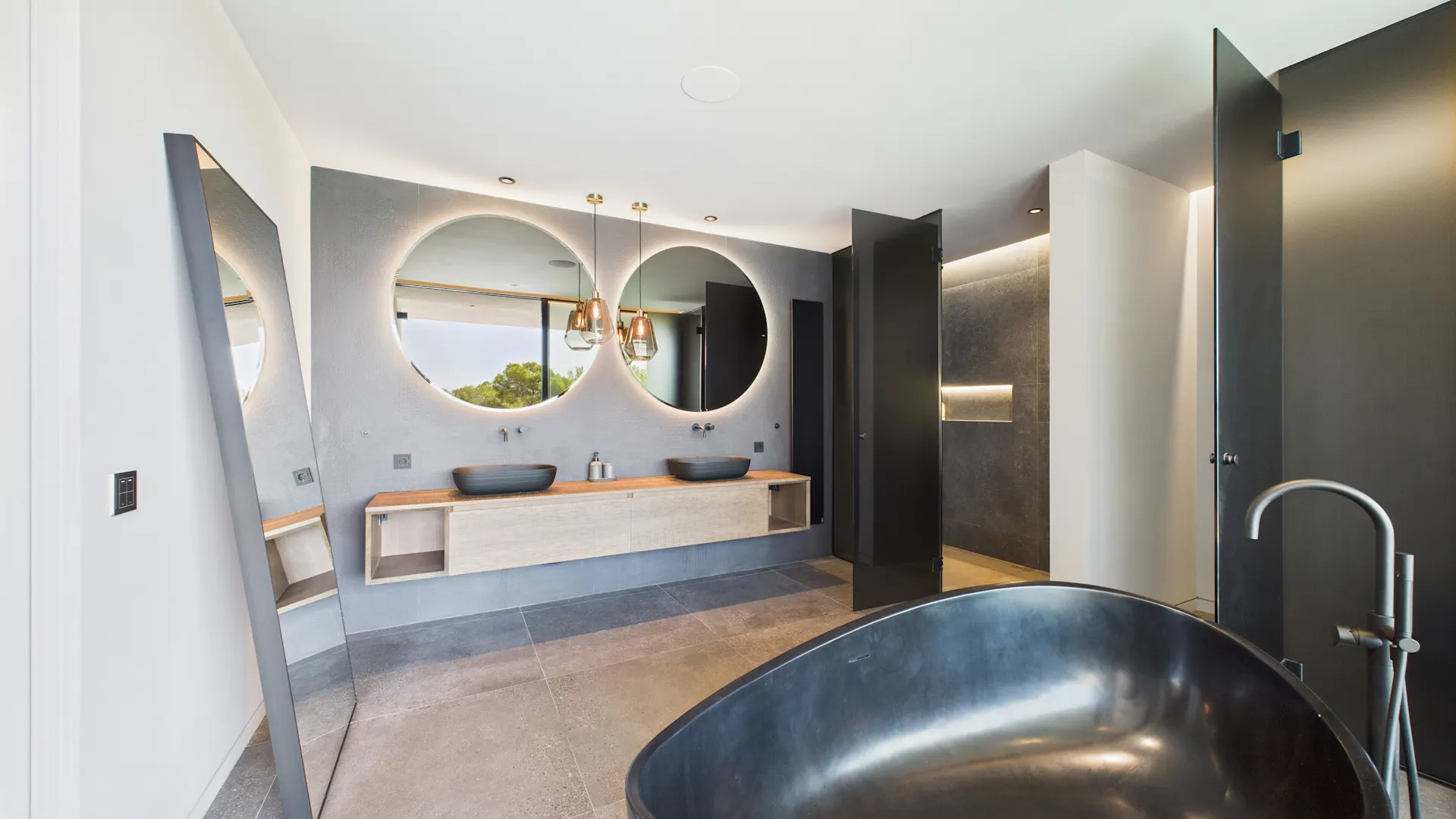 Modernes Badezimmer mit freistehender Badewanne, zwei runden Spiegeln und Doppelwaschbecken.
