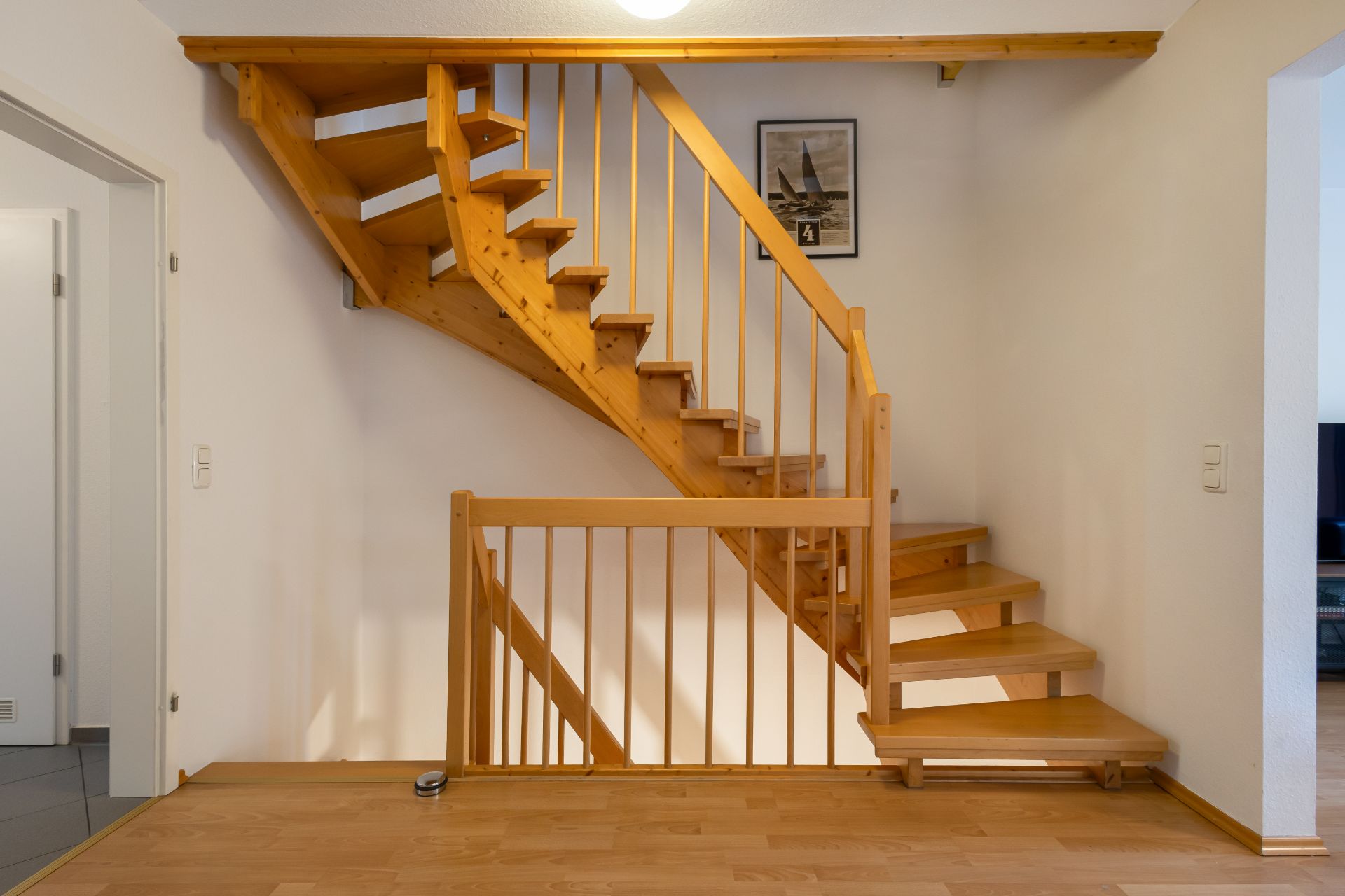 Holztreppe mit Geländer in einem Wohnraum, helles Parkett und ein Bild an der Wand.