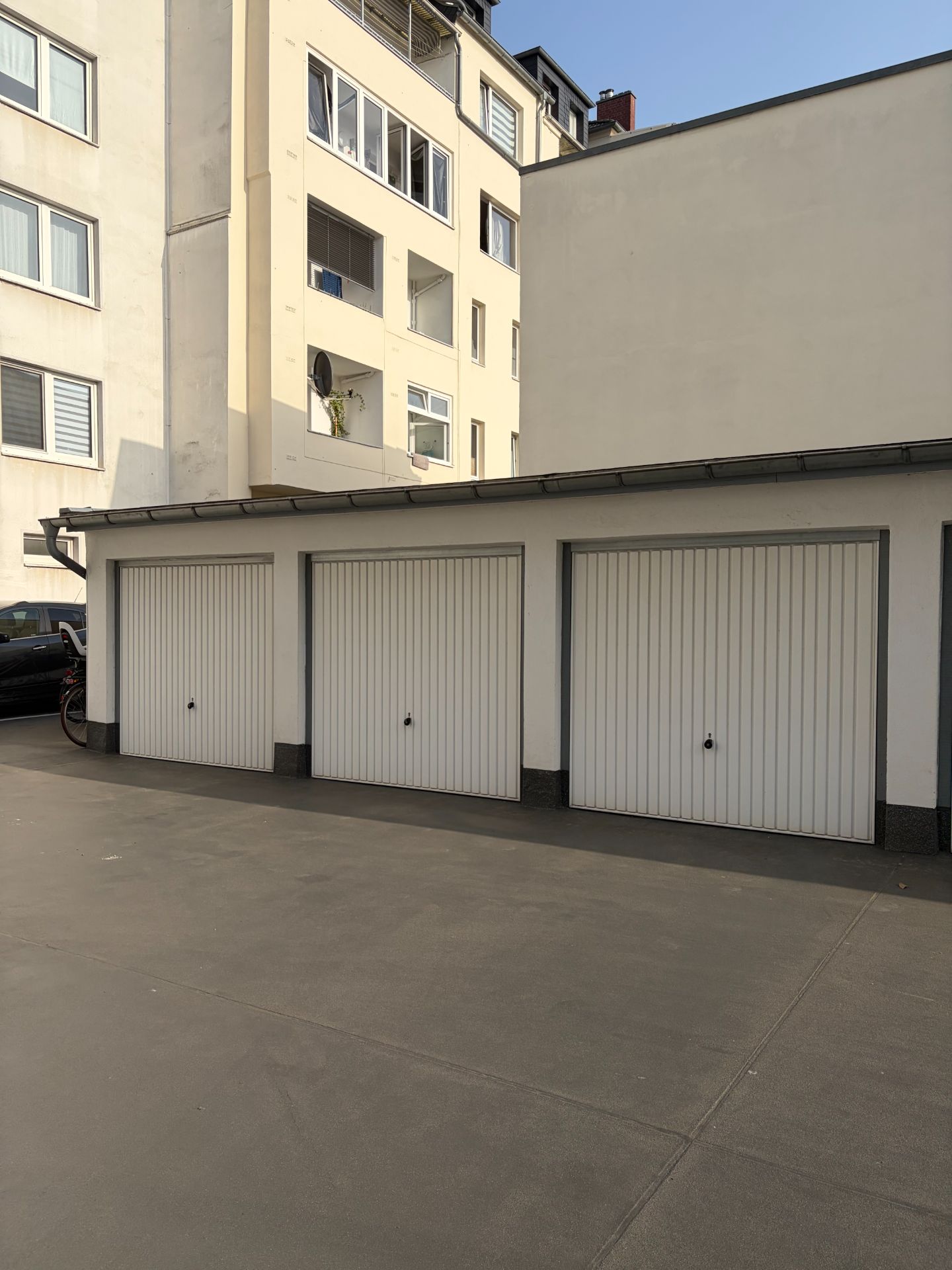 Drei geschlossene Garagentore vor einem mehrstöckigen Wohngebäude.