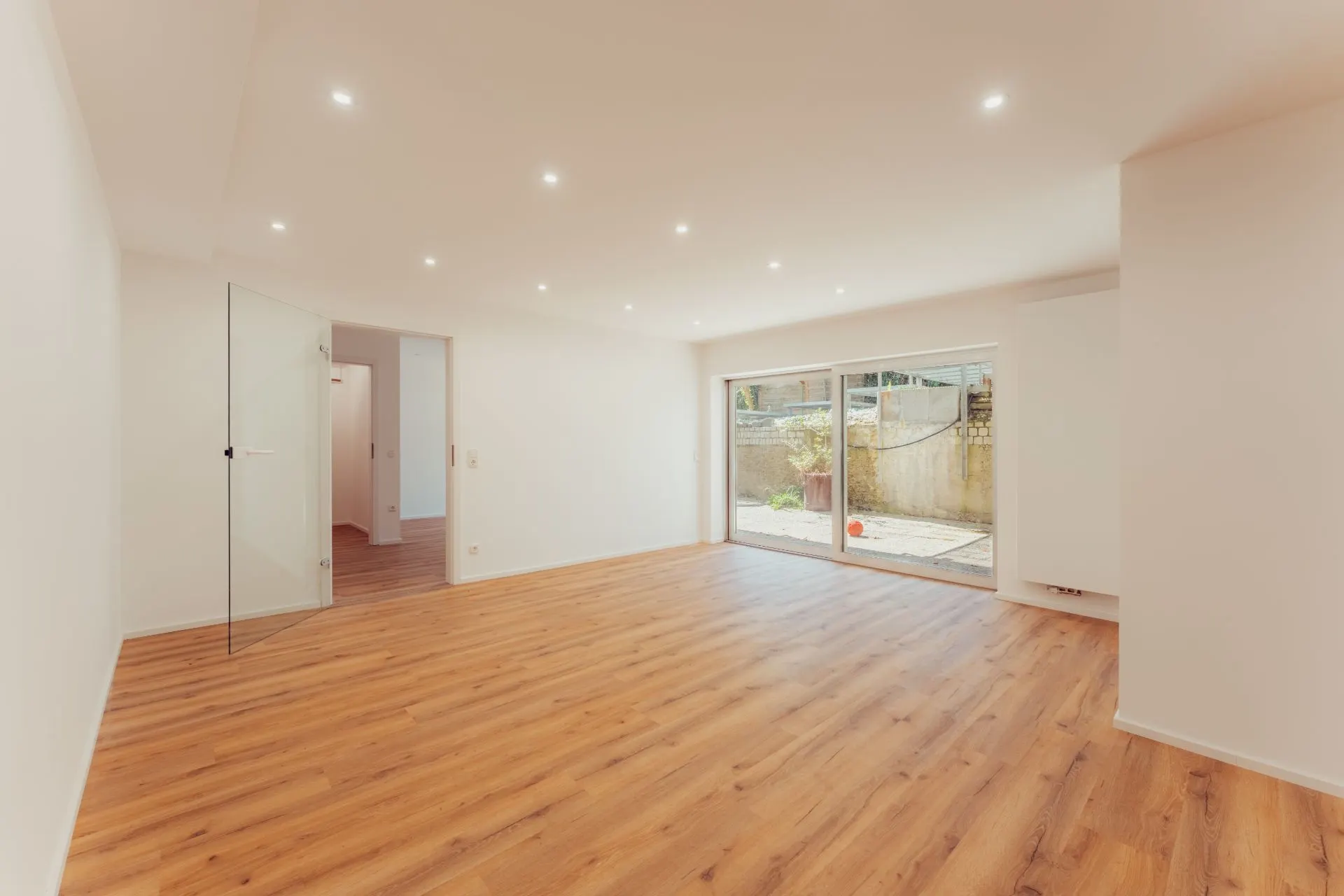 Helles Wohnzimmer mit Holzfußboden, Spotlichtern und großer Glastür zum Garten.