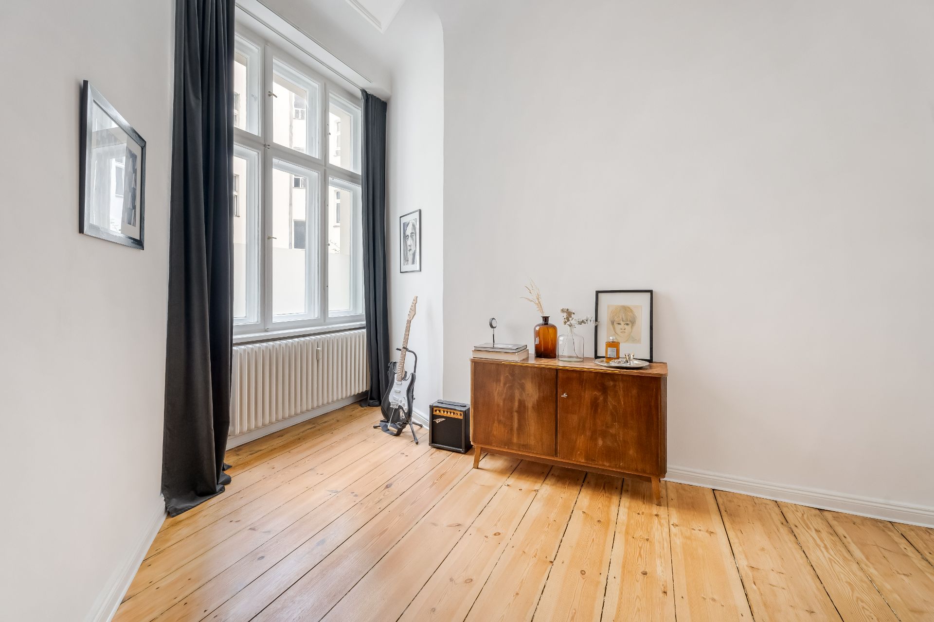 Helles Zimmer mit Holzboden, großem Fenster, Gitarre und Kommode mit Dekoration.