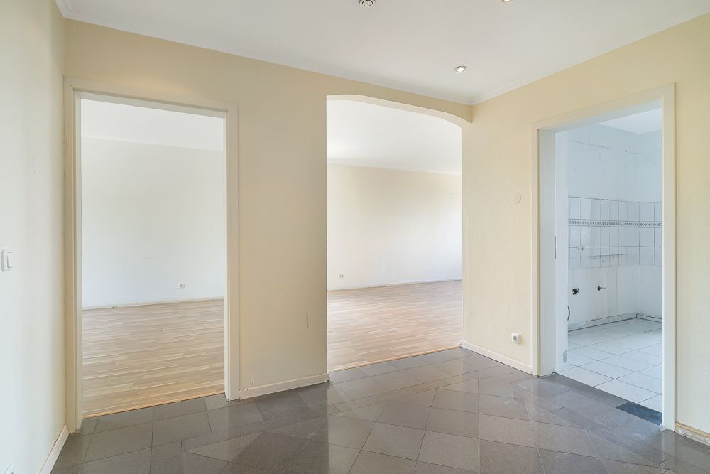 Flur mit Blick in ein Wohnzimmer mit Holzboden und eine Küche mit weißen Fliesen.