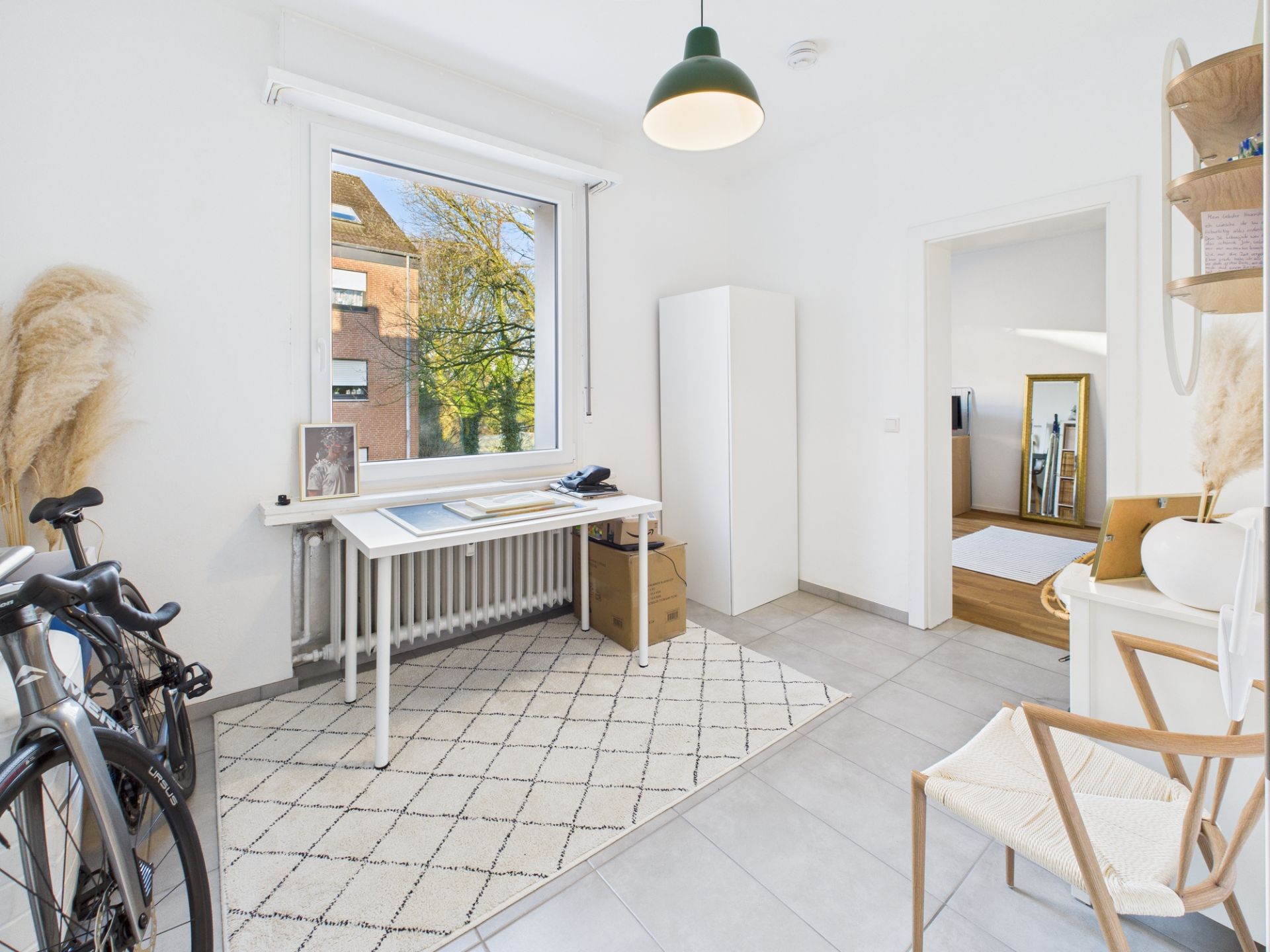 Helles Arbeitszimmer mit Schreibtisch, Fahrrad, Teppich und großem Fenster.