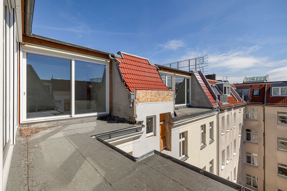 Dachterrasse mit Zugang zu mehreren Wohnungen und roten Dachziegeln bei Tageslicht.