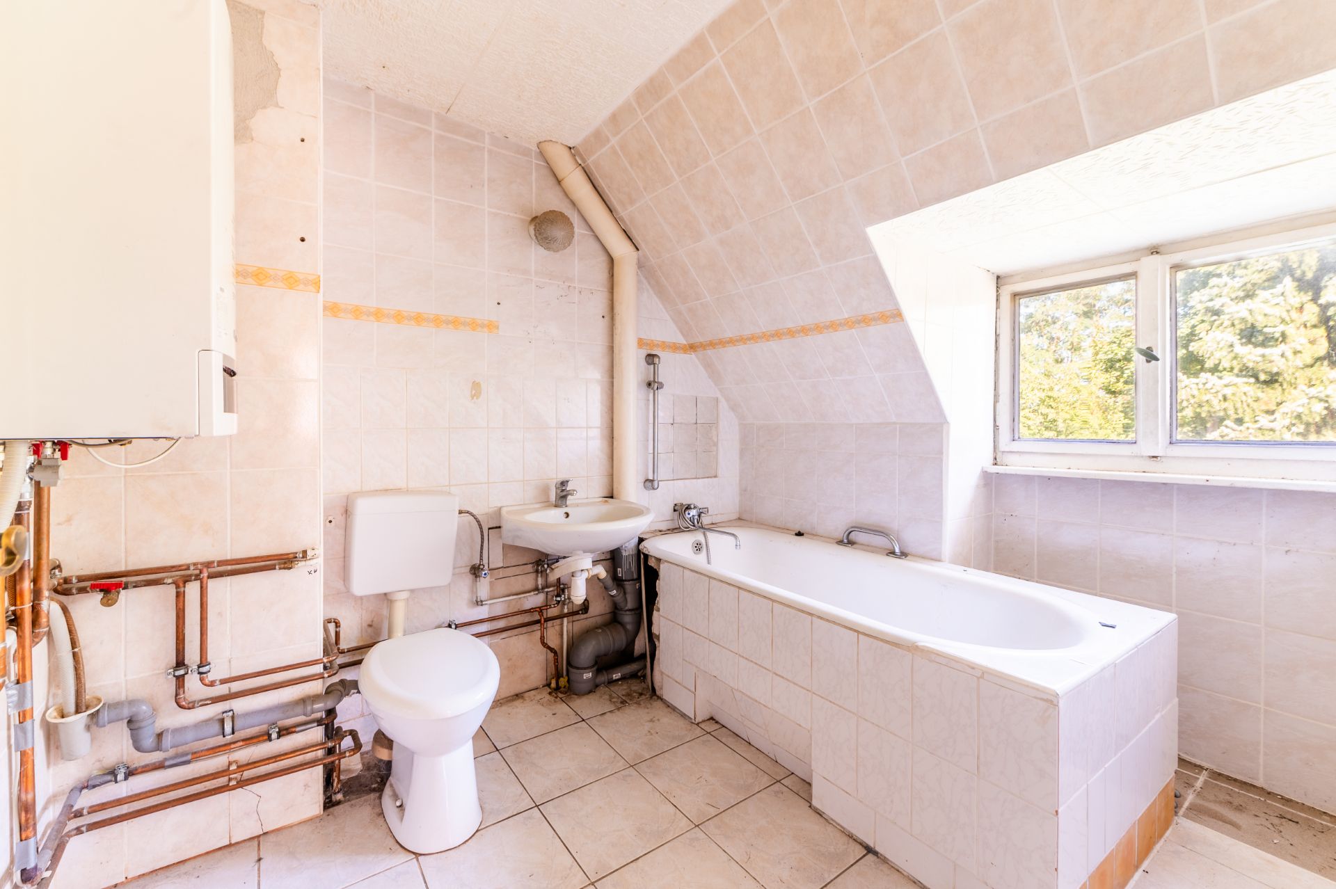 Helles Badezimmer mit Toilette, Waschbecken, Badewanne und Fenster unter Dachschräge.