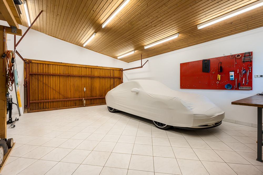 Garage mit Auto unter Abdeckung, Werkzeugwand und Holztor.