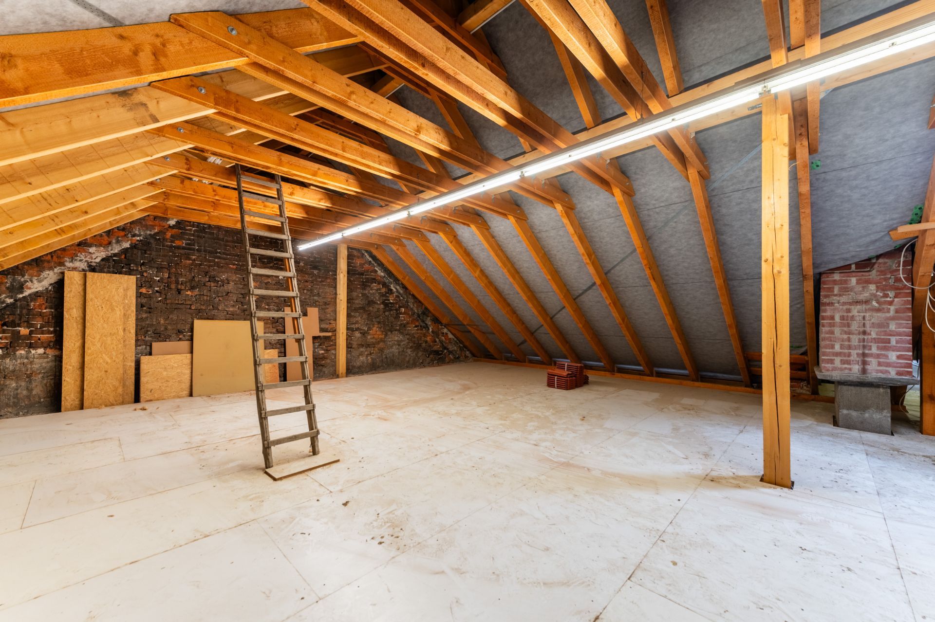 Heller Dachboden mit Holzbalken, Leiter und Dachschrägen, teils mit Baumaterialien gelagert.