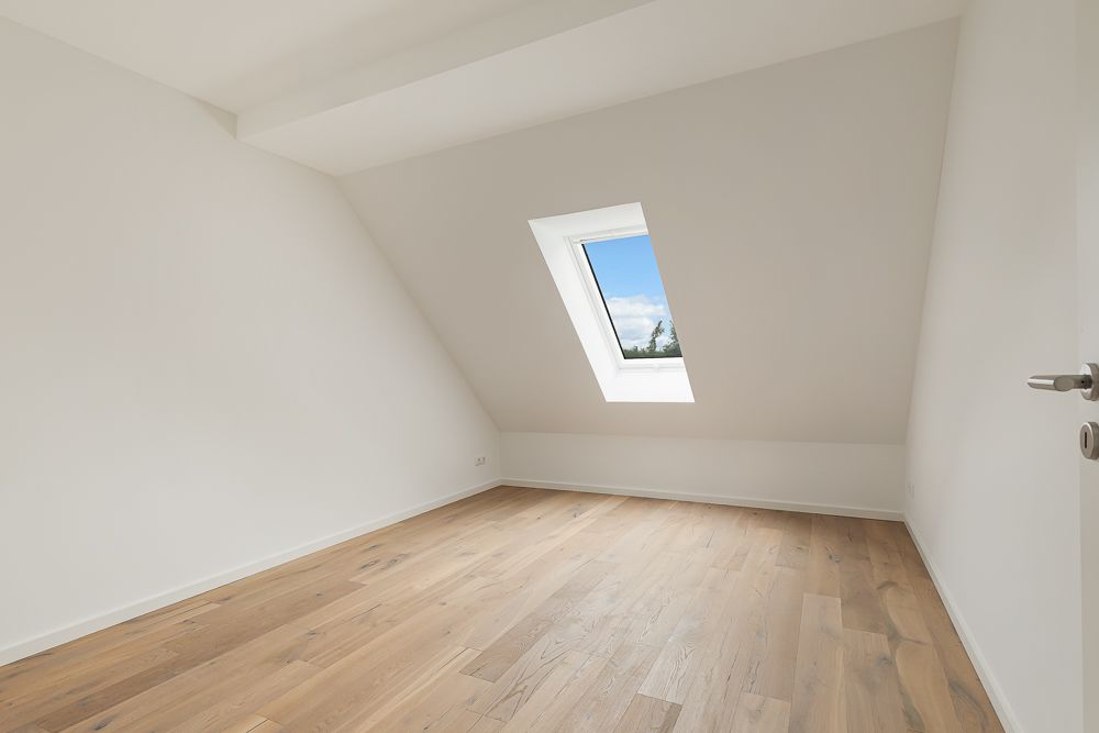Leerer, heller Raum mit schräger Decke, Dachfenster und Holzfußboden.