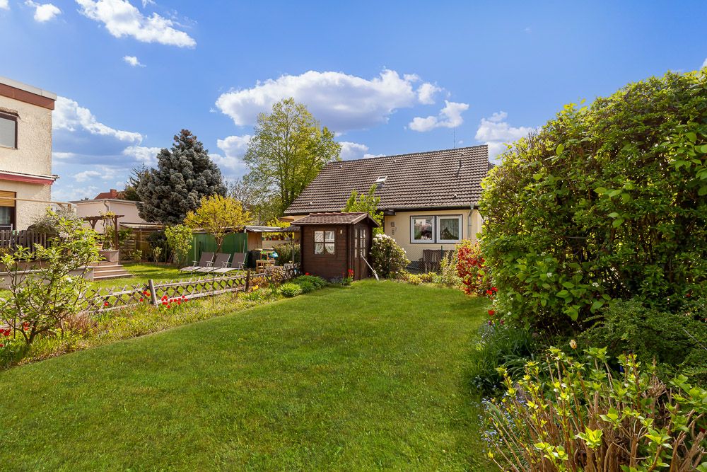 Garten mit Rasen, kleinen Sträuchern und einem Holzhaus vor einem Wohnhaus.