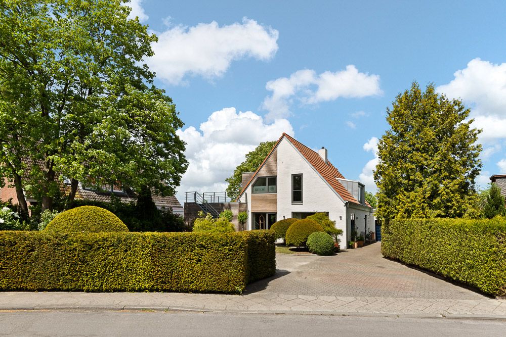 Modernes Einfamilienhaus mit schrägem Dach, grüner Hecke und gepflegtem Vorgarten.