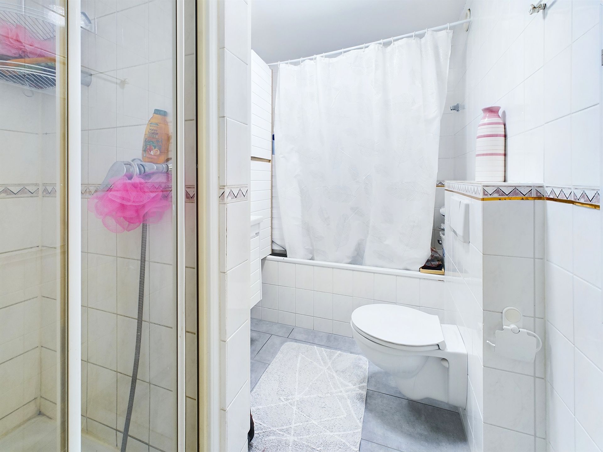 Helles Badezimmer mit Dusche, Toilette, Badewanne mit Duschvorhang und weißem Fliesenboden.