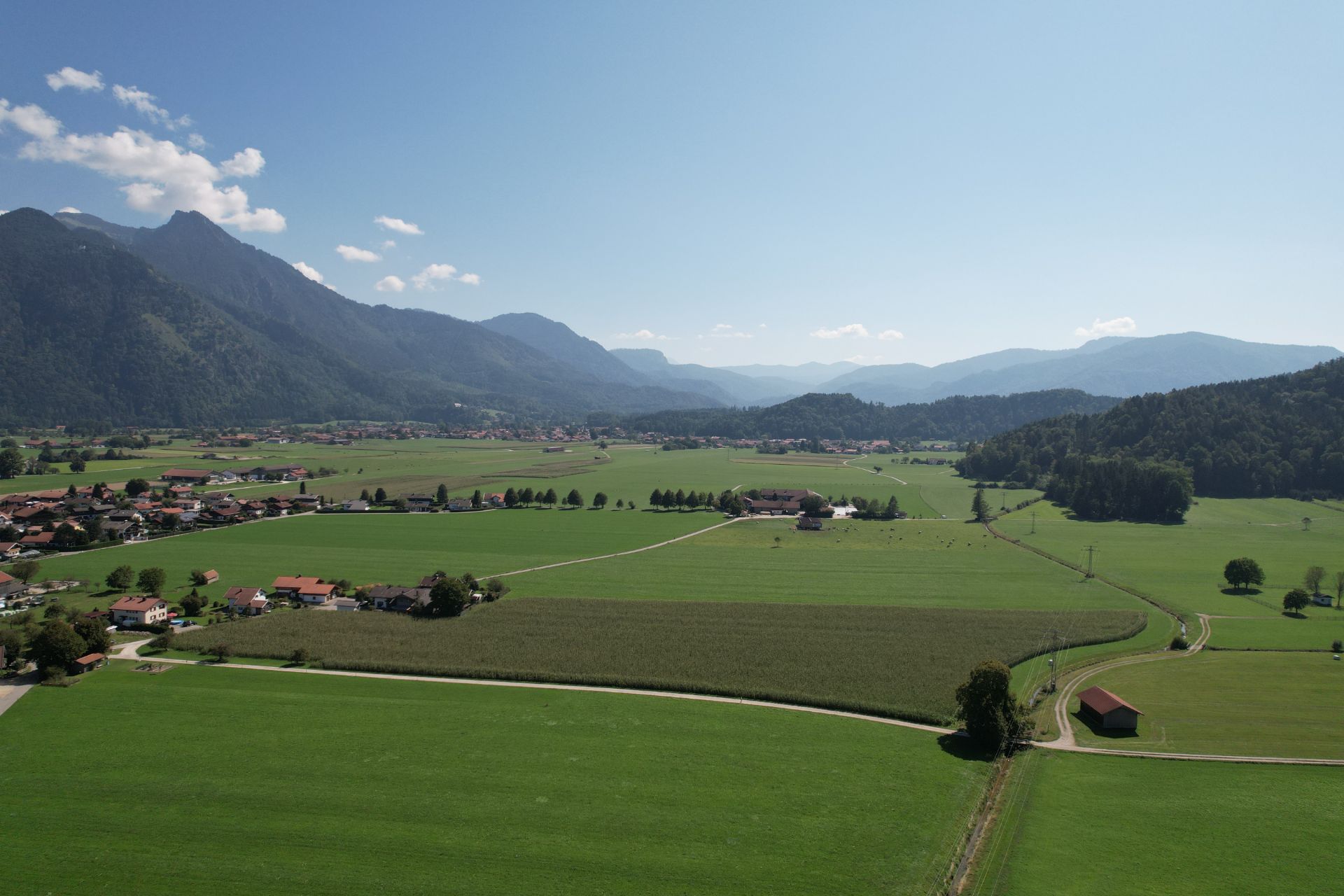 Luftaufnahme von grünen Feldern, kleinen Häusern und Bergen im Hintergrund.