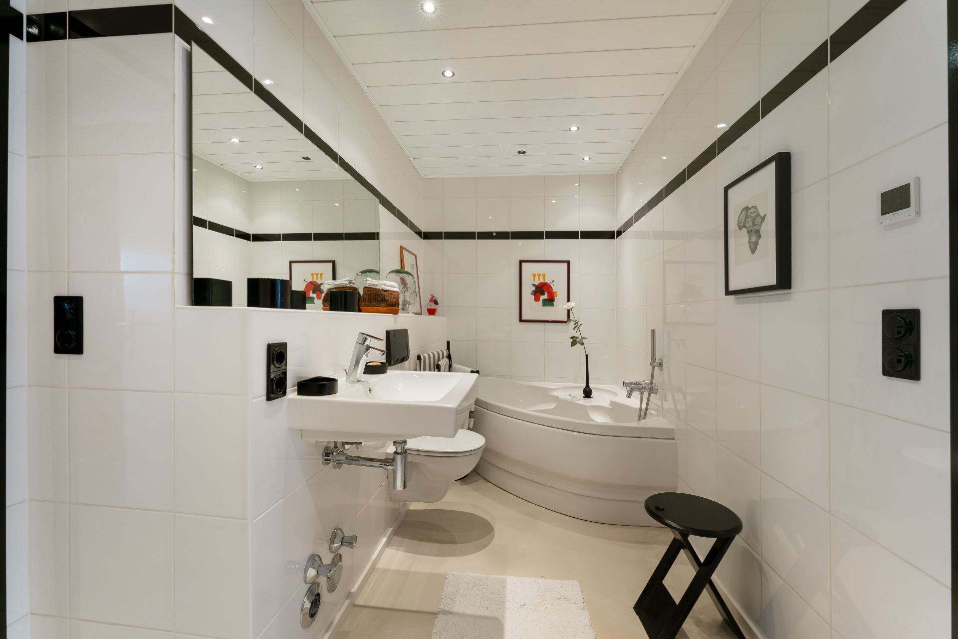 Modernes Badezimmer mit Eckbadewanne, Waschbecken, Hocker und Wandbildern.