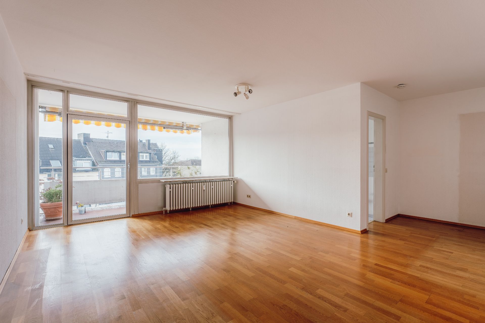 Helles Wohnzimmer mit Parkettboden, großen Fenstern und Zugang zu einem Balkon.