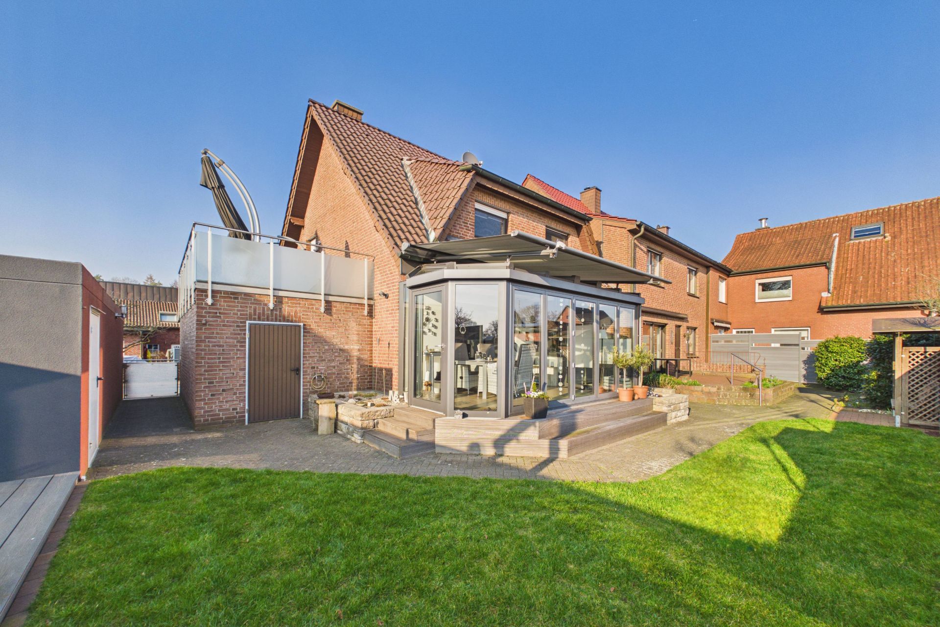 Backsteinwohnhaus mit Wintergarten und gepflegtem Garten bei sonnigem Wetter.