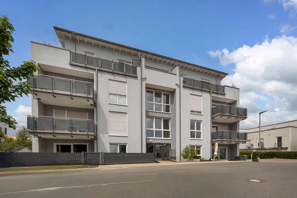 Modernes, dreistöckiges Wohnhaus mit mehreren Balkonen und großem Eingangsbereich.