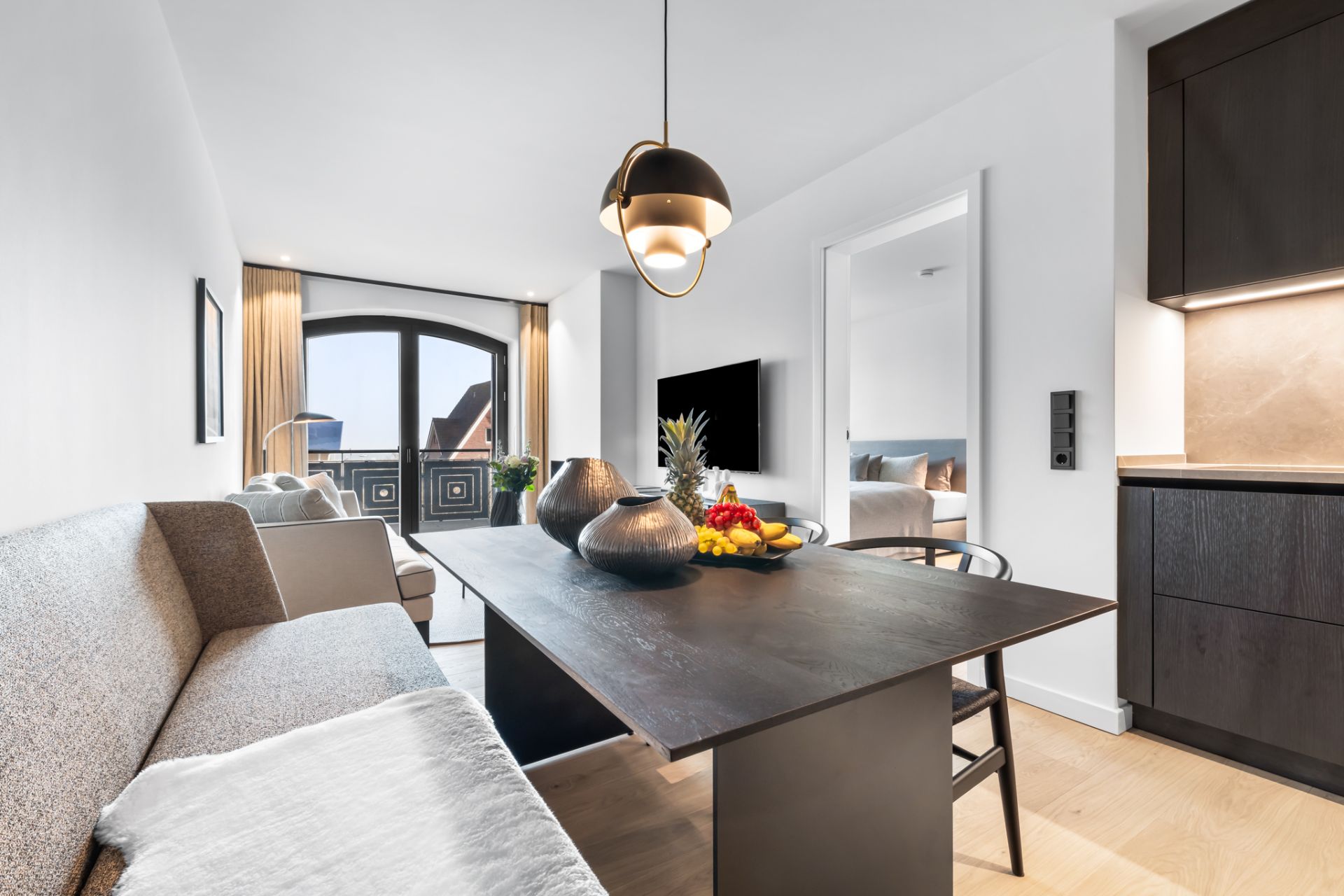 Modernes Esszimmer mit dunklem Tisch, Sofa, Obstschale und Blick auf einen Balkon.