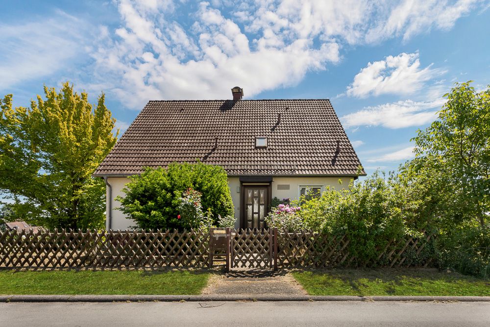 Ein Einfamilienhaus mit Garten, Holzzaun und Bäumen vor blauem Himmel.