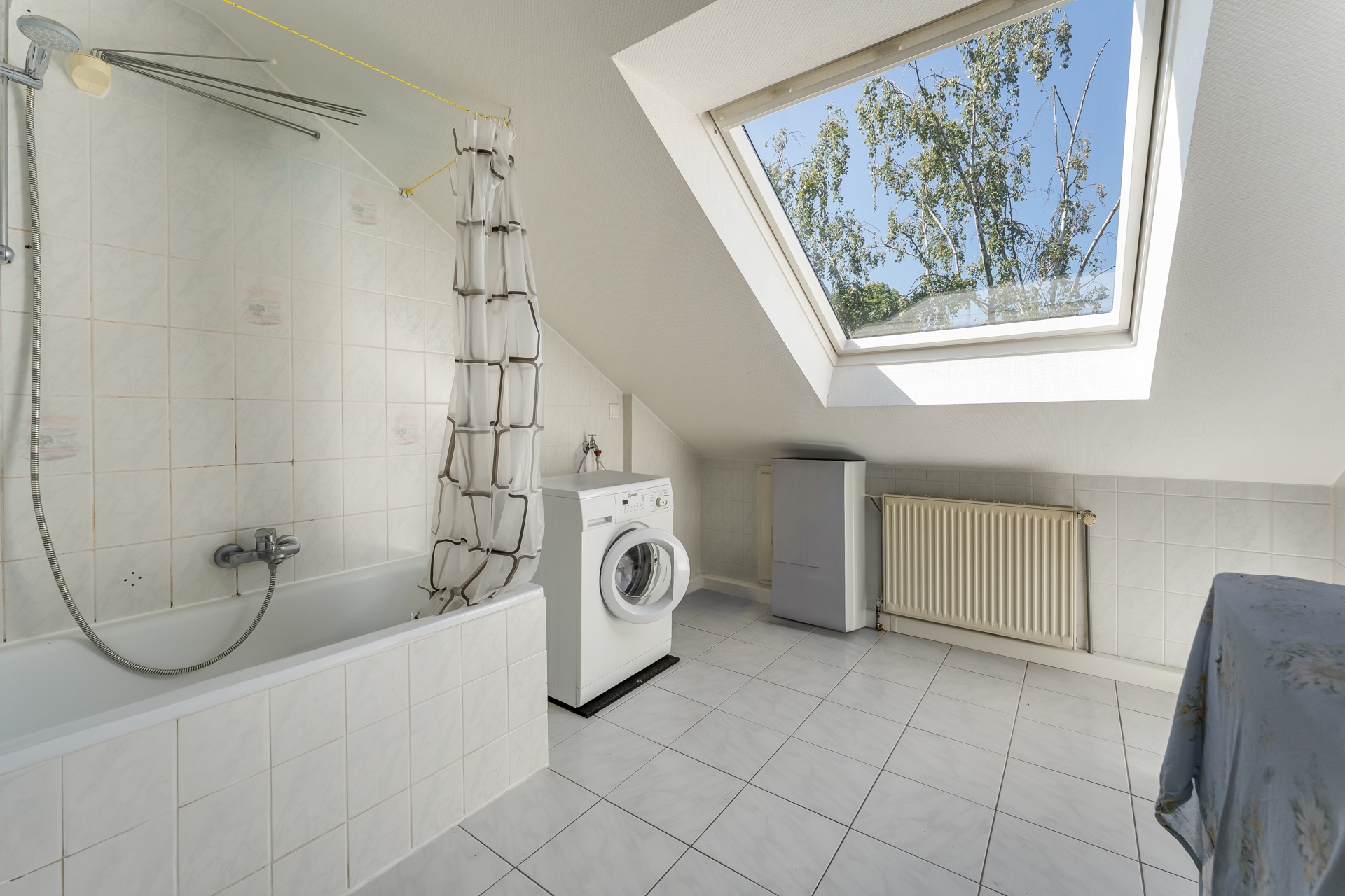Badezimmer mit Badewanne, Waschmaschine und großem Dachfenster unter einer Schräge.